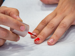 A woman painting her nails with red nail polish. Beauty salon cosmetic treatments. Close up of girl hands and nails with paint brush.