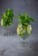 Summer mint lime refreshing cocktail mojito with rum and ice in glass on gray background. Mojito cocktail on stone table. Glassy high glass for drinks. Lemonade at the bar.