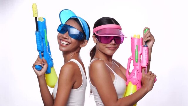 Portrait of two beautiful Asian women in pink and blue sun visor cap and sunglasses posing with water guns over white background - video in slow motion