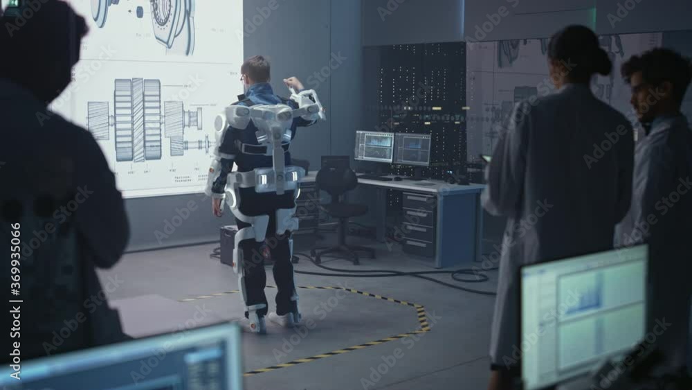 Poster In Development Laboratory: Engineers and Scientists Look at Robotics Exoskeleton Prototype Presentation with Person Testing it, Moving and Performing. Designing Wearable Exosuit to Help People