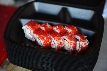 Pieces of sushi with cream cheese and red tobiko caviar in a black food container, close-up.