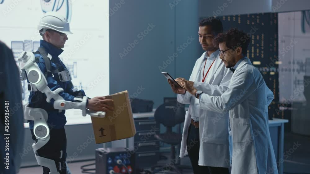 Aufkleber In Development Laboratory: Engineers Look at Robotics Exoskeleton Prototype Presentation with Person Testing it, Lifting Heavy Carboard Box. Designing Wearable Exosuit to Help Warehouse Workers