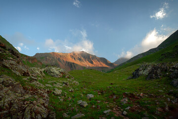 mountain meadow with green grass and stones and the top of the mountain illuminated by the setting sun