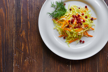 Fresh cabbage salad made from shredded white cabbage, carrots and berries on a white plate. Top view, wooden background, selective focus