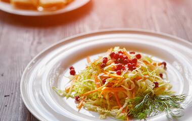Fresh cabbage salad made from shredded white cabbage, carrots and berries on a white plate. Top view, wooden background, selective focus