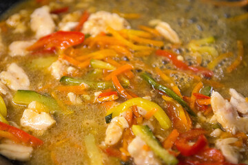 Chopped vegetables and pieces of chicken fillet are stewed in a pan, close-up. Cooking food.