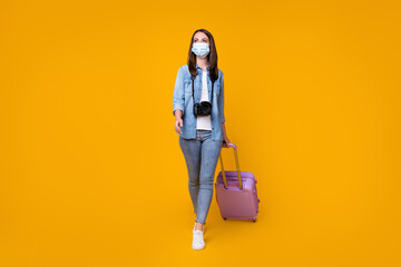 Full length photo of pretty lady hold rolling bag camera photographer travel airport quarantine walk registration wear facial mask casual denim shirt shoes isolated yellow color background