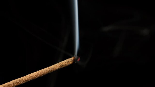 sandalwood stick with incense smokes on a black background, close-up