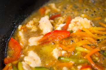 Chopped vegetables and pieces of chicken fillet are stewed in a pan, close-up. Cooking food.