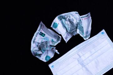 a crumpled one thousand ruble bill on a black background with a medical mask symbolizing a fall in...