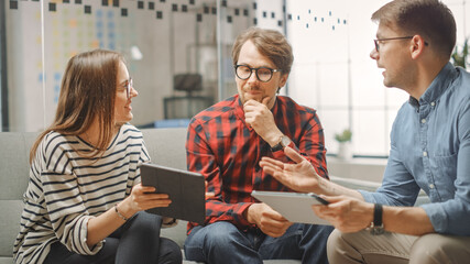 Young Woman and Two Male Colleagues Having a Friendly Meeting and Discussing New Business Ideas. Easygoing Coworking Atmosphere in Loft Office Creative Agency. They Look at Papers and Tablet.