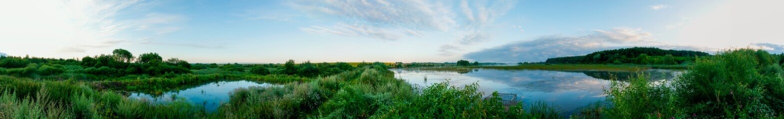 Panoramic landscape from the lake with colorful clouds in the summer sun.