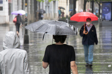 People under umbrellas walking the pedestrian street on a rainy summer day in the city