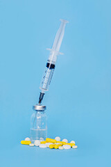 a syringe stuck in a medicine bottle and a lot of pills near by on a blue background