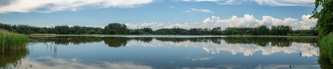 panorama mirrored blue sky with white clouds and forest in a lak