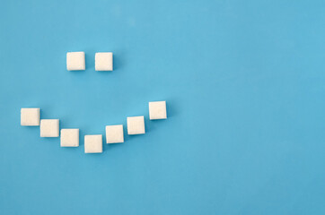 White sugar cubes laid out in the form of a smile on a blue background close-up, copy space. Concept of health, dentistry
