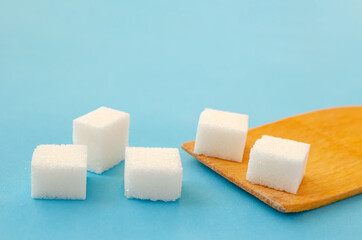 Sugar cubes lie on a wooden spoon and a blue background, copy space