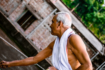 Close-up Portrait of Indian Senior Man Arching. Happy alone side facing old man, wearing white dress, giving pose with style at the camera. Elderly Man Is Enjoying Retirement In Nature In Afternoon.