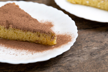 sponge cake with cream and milk brown chocolate decorate. Sliced piece of cake on white plate. Served on wooden table. Favorite dessert for celebrate event or birthday party.