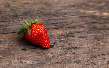 One strawberry on golden fork on wooden non paint background