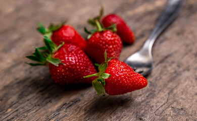 Fresh strawberries and one berry on fork still life on dark wooden background. Organic garden strawberry on rustic.