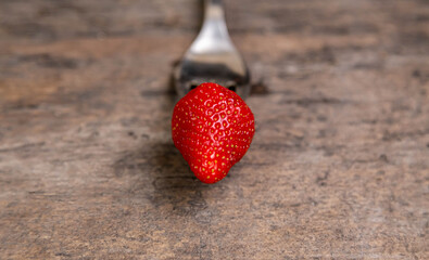One strawberry on golden fork on wooden non paint background