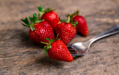 Fresh strawberries and one berry on fork still life on dark wooden background. Organic garden...