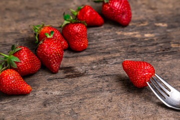 Fresh strawberries and one berry on fork still life on dark wooden background. Organic garden strawberry on rustic.