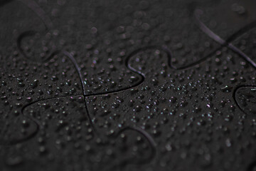Macro view of black jigsaw puzzle pieces with water droplets and selective focus