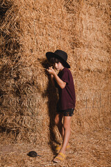 Naklejka na ściany i meble A cute young boy with a hat in a straw bale in a romantic and warm summer night in a rural environment.