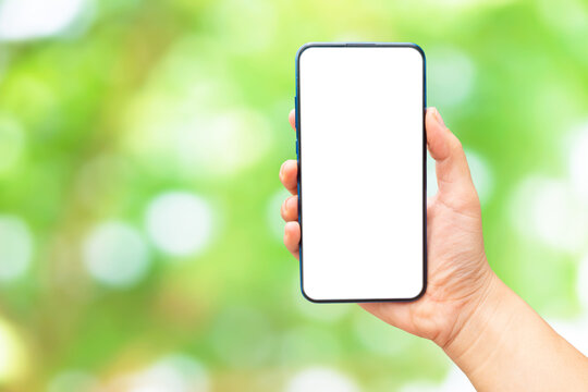 Mock up image of A hand holding a blank screen of smartphone on green bokeh blurred​ background.