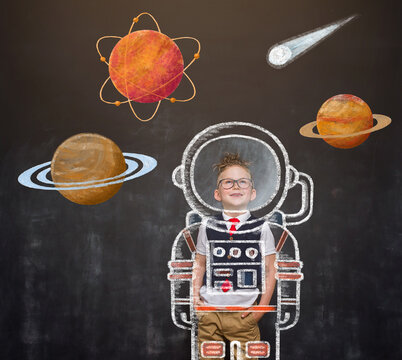 Childhood. Nerd kid boy dreams about future. School boy astronaut in space suit with pictures of space and planets on blackboard. Rocket and win concept. Innovation