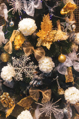 The artificial Christmas tree is decorated with gold and silver decorative soft toys: flowers, snowflakes, bows.