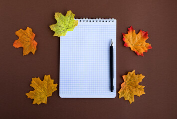 School notebook pen white alarm clock multicolored autumn leaves on a brown background. back to school concept. flat lay. copy space
