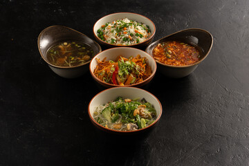 Symmetrical composition of an-asian and pan-asian cuisine on a stylish black concrete kitchen table, soups, rice, egg noodles, glass noodles and vegetables garnishes.