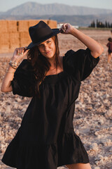 dark haired European woman with a black hat in a black dress in the countryside