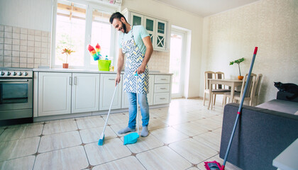 Happy handsome young beard man is cleaning the floor in the domestic kitchen and have fun.