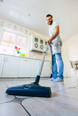 Happy handsome young beard man is cleaning the floor in the domestic kitchen and have fun.