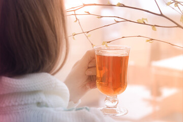 A girl in a white hat is drinking tea on the balcony in the spring. The leaves are blooming. Spring, Sunny mood of a woman on a woman's day.