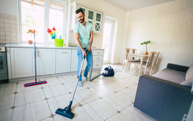 Happy handsome young beard man is cleaning the floor in the domestic kitchen and have fun.