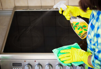 Beautiful young woman in casual wear is wiping electrical stove in the kitchen while cleaning her house.