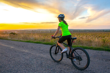 Fototapeta na wymiar Beautiful girl cyclist riding a bike on the road towards the sunset. Nature and recreation. Hobbies and sports