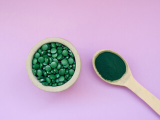 Green hawaiian spirulina in tablespoons pills and powder on light lilac background. Super food, healthy lifestyle, healthy supplements concept