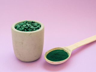 Green hawaiian spirulina in tablespoons pills and powder on light lilac background. Super food, healthy lifestyle, healthy supplements concept