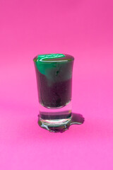 Liquid spirulina green drink in short cocktail glass and spirulina pills on pink background