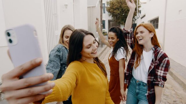 Young woman taking a selfie video with friends dancing outdoors. Group of women enjoying dancing on the street and taking a selfie.
