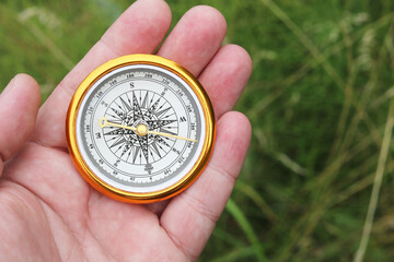 Old classic navigation compass in hand on natural background as symbol of tourism with compass,...
