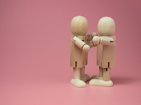 2 wooden dolls hugging each other on a pink background. Concept of social contact from wooden dolls. - Powered by Adobe