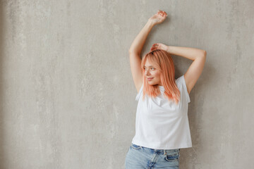 Young joyful woman in white t-shirt with dyed hair posing at wall with raised hands