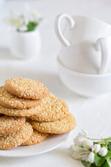 Freshly baked round sesame cookies with a apple tree flowers and three tea cups on a white table.